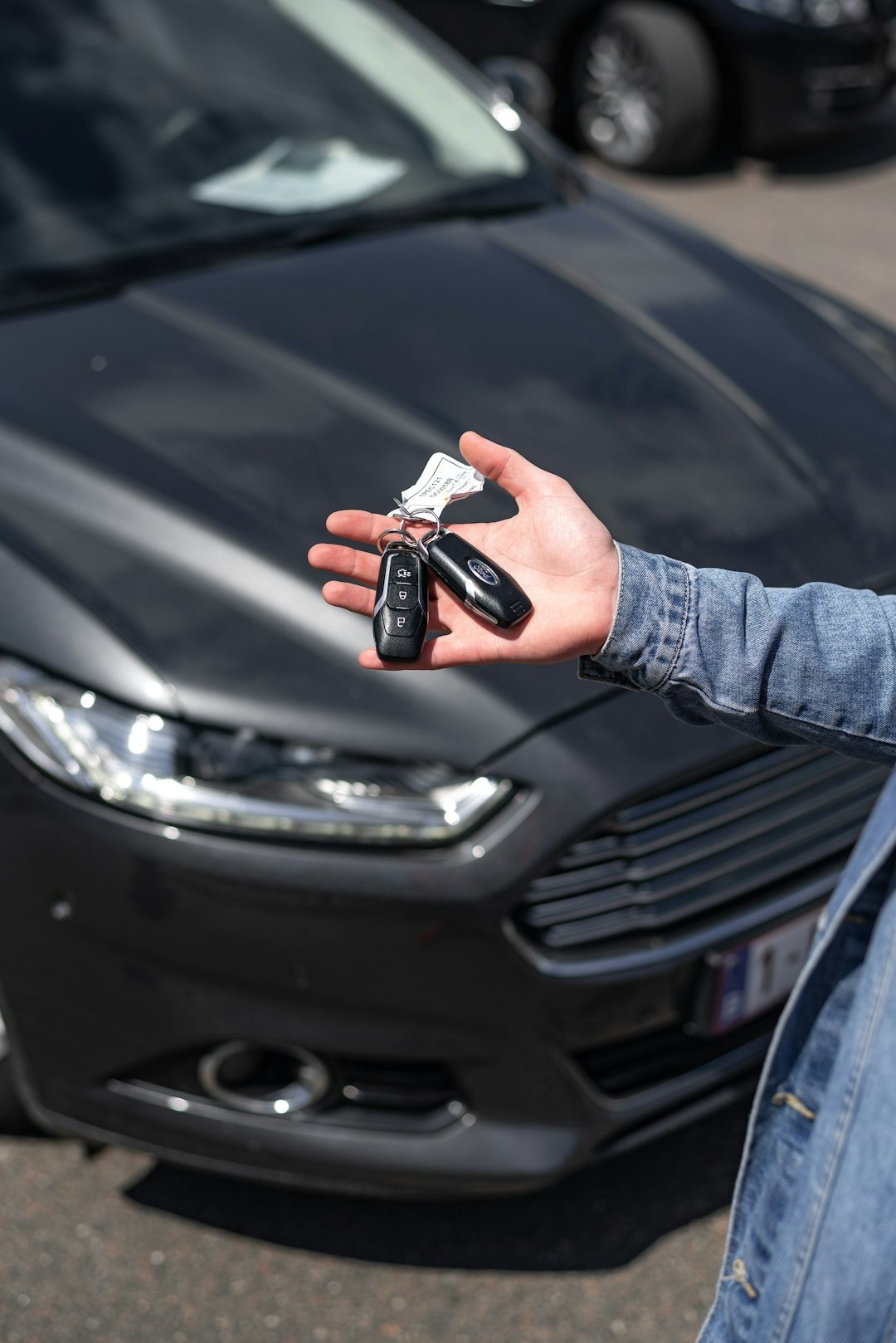 Hand holding two car key fobs towards the camera.